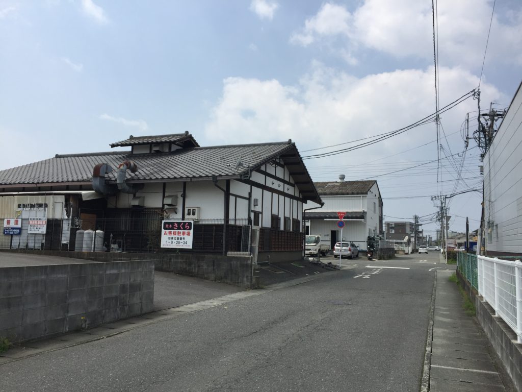さらに100メートルほど曲がらずに直進します。 道が横切る左手前に建物があり、その手前に駐車場の入り口があります。No.21に駐車してください。
