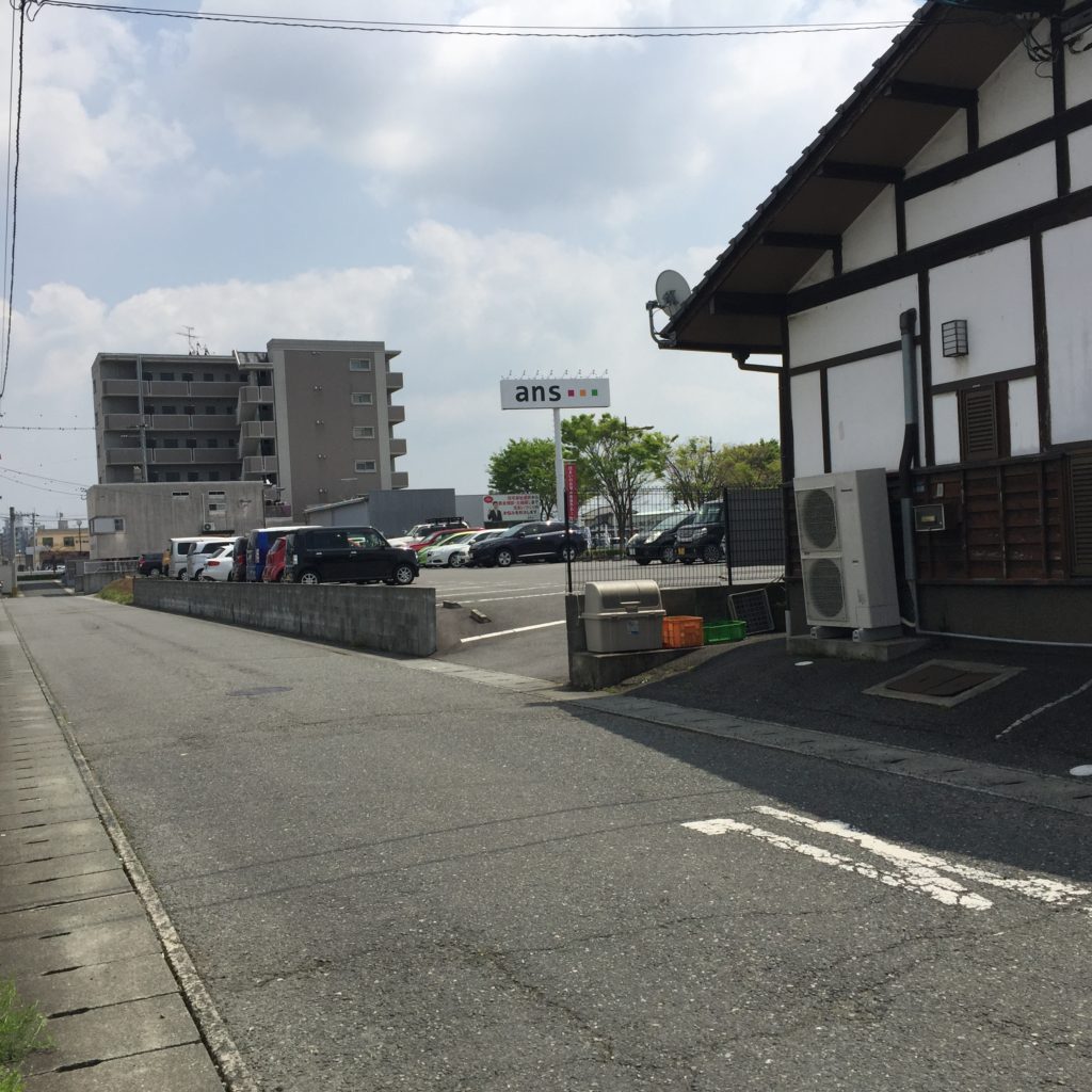 横の道を右折すると裏に駐車場の入り口があります。奥に見える6階建てのマンションです。